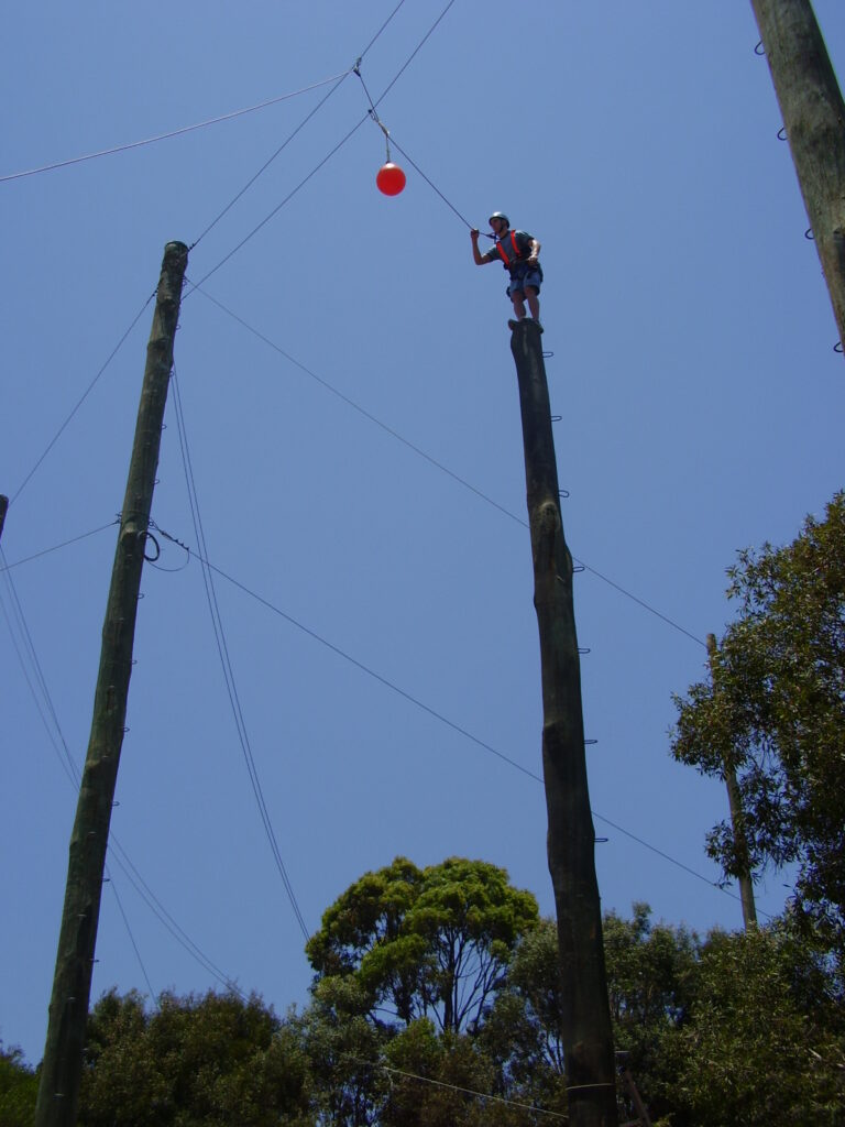 Adventurer jumping off high metre rope column to hit a ball in leap of faith
