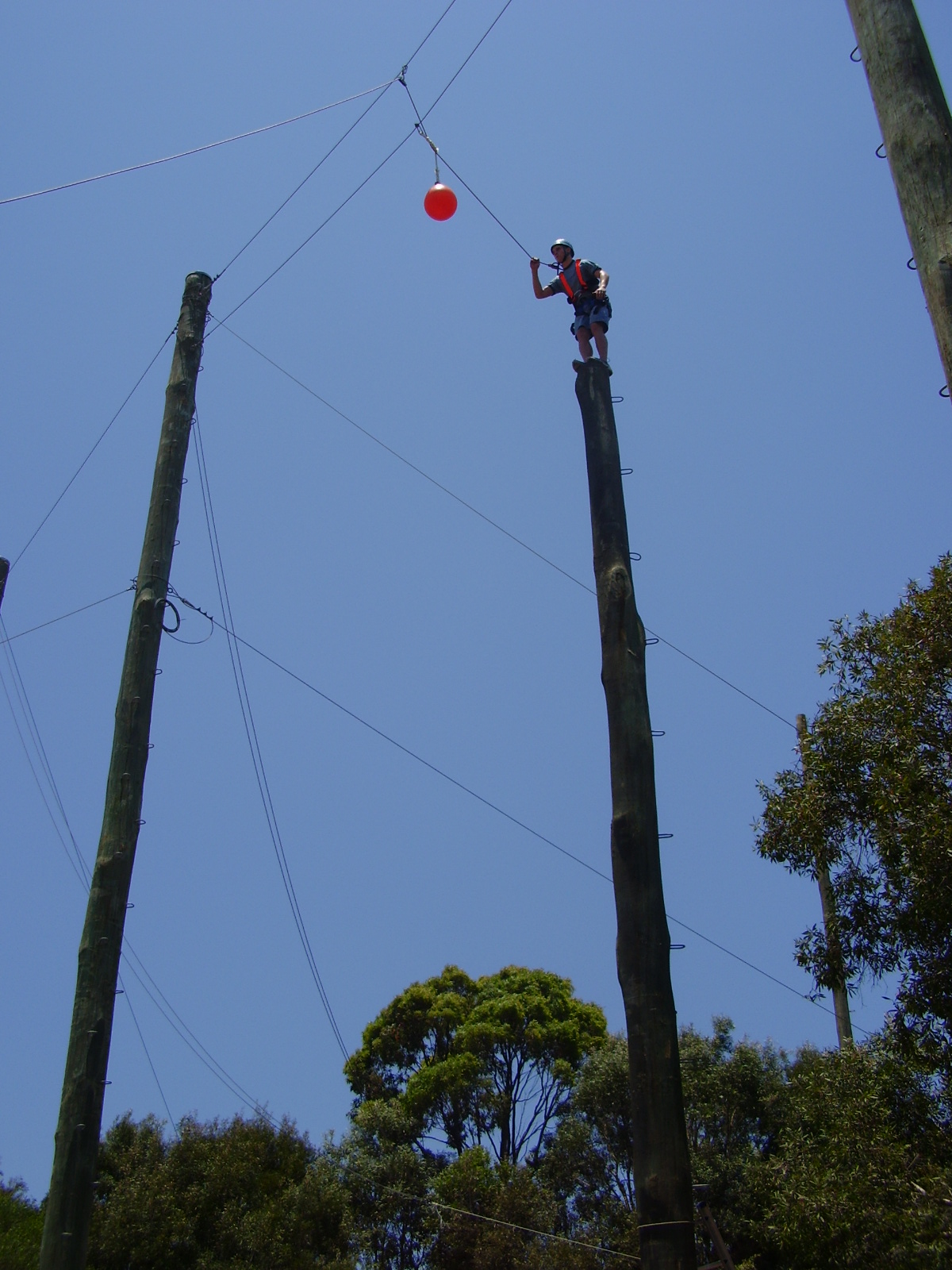Adventurer jumping off high metre rope column to hit a ball in leap of faith